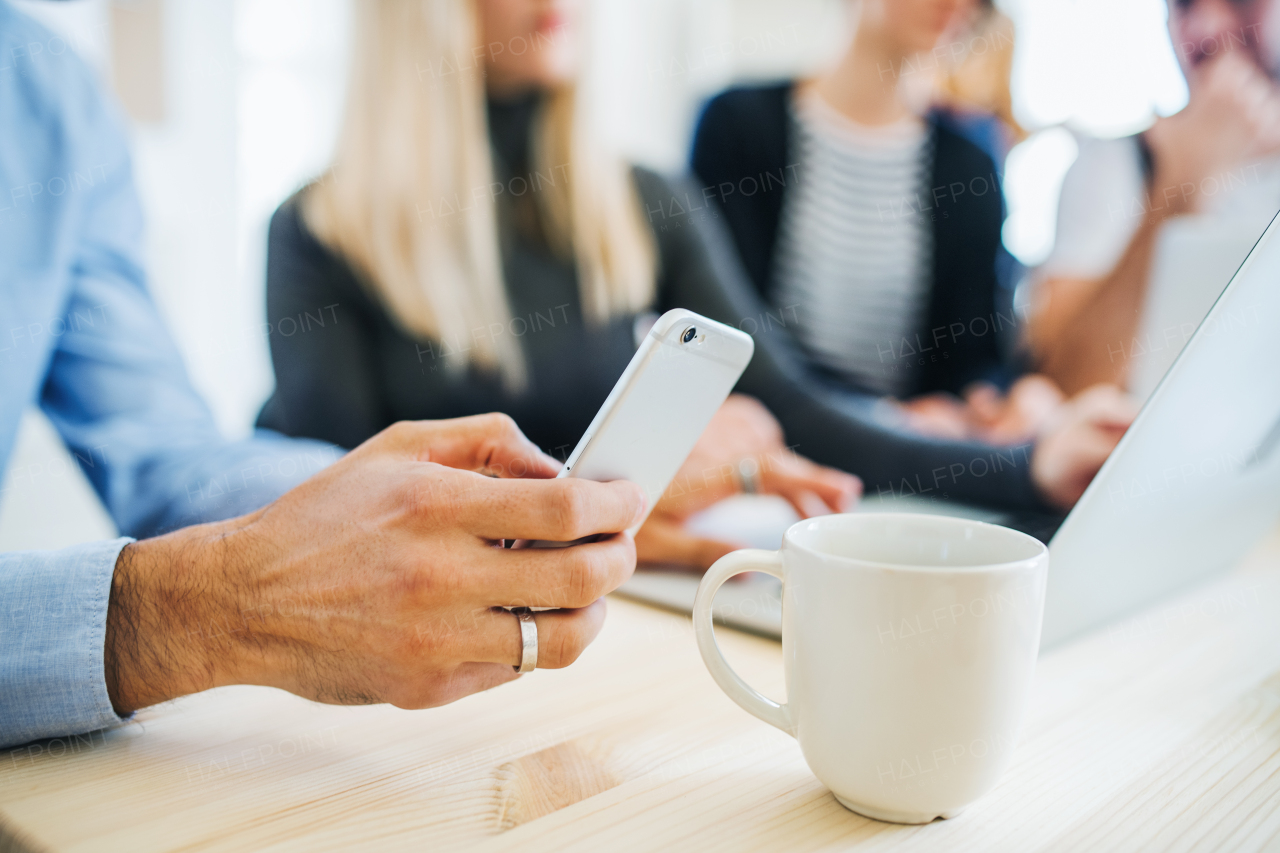 Group of young, male and female businesspeople with smartphone and tablet working together in a modern office, a midsection view.