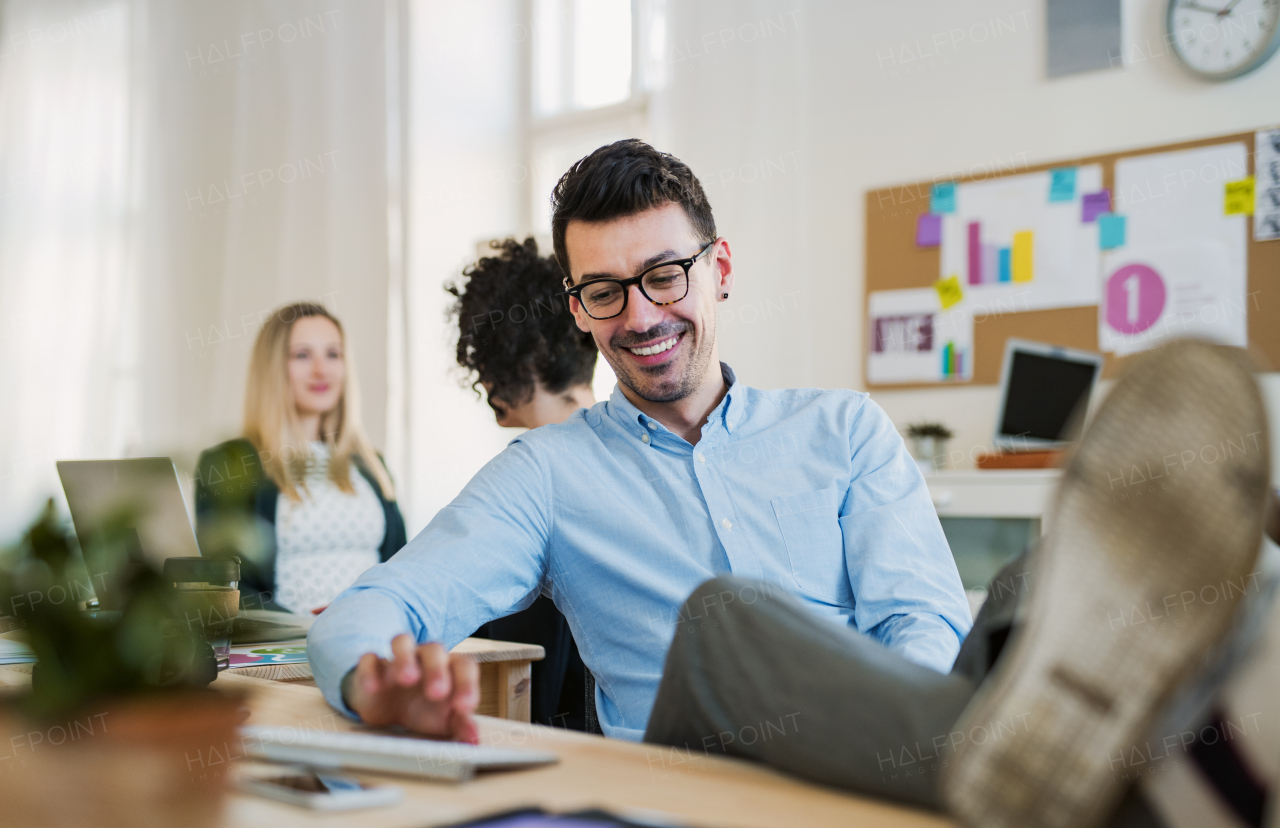 A portrait of young businessman with colleagues in a modern office, feet on table.