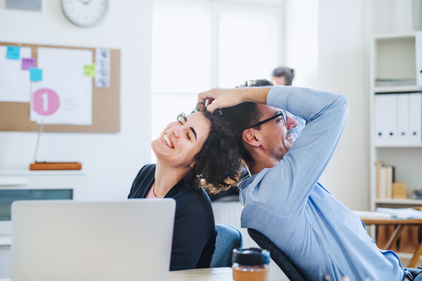 Two young cheerful businesspeople relaxing in a modern office, laughing.