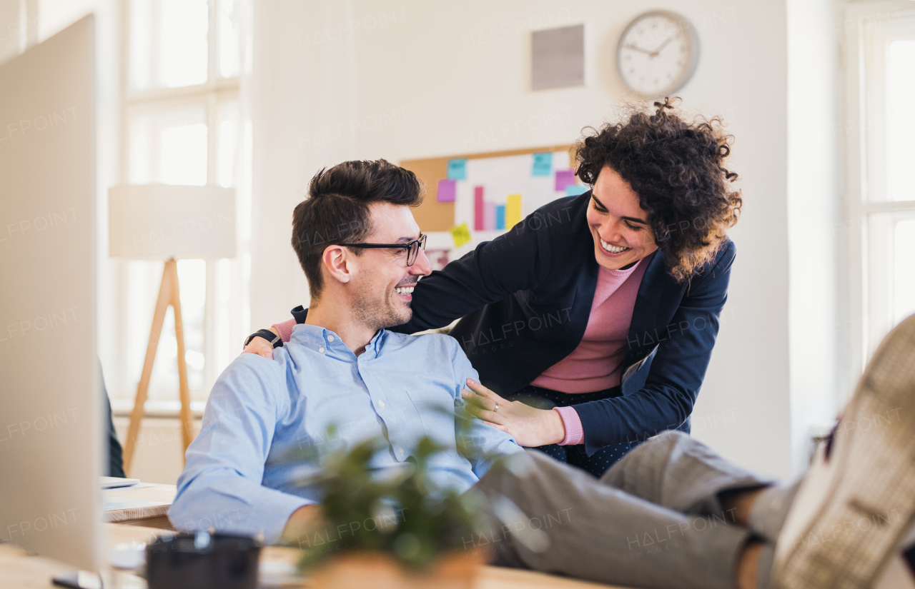 Two young cheerful businesspeople working together in a modern office, feet on a desk.