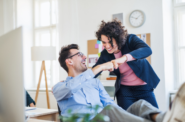 Two young cheerful businesspeople in a modern office, making a fist bump.