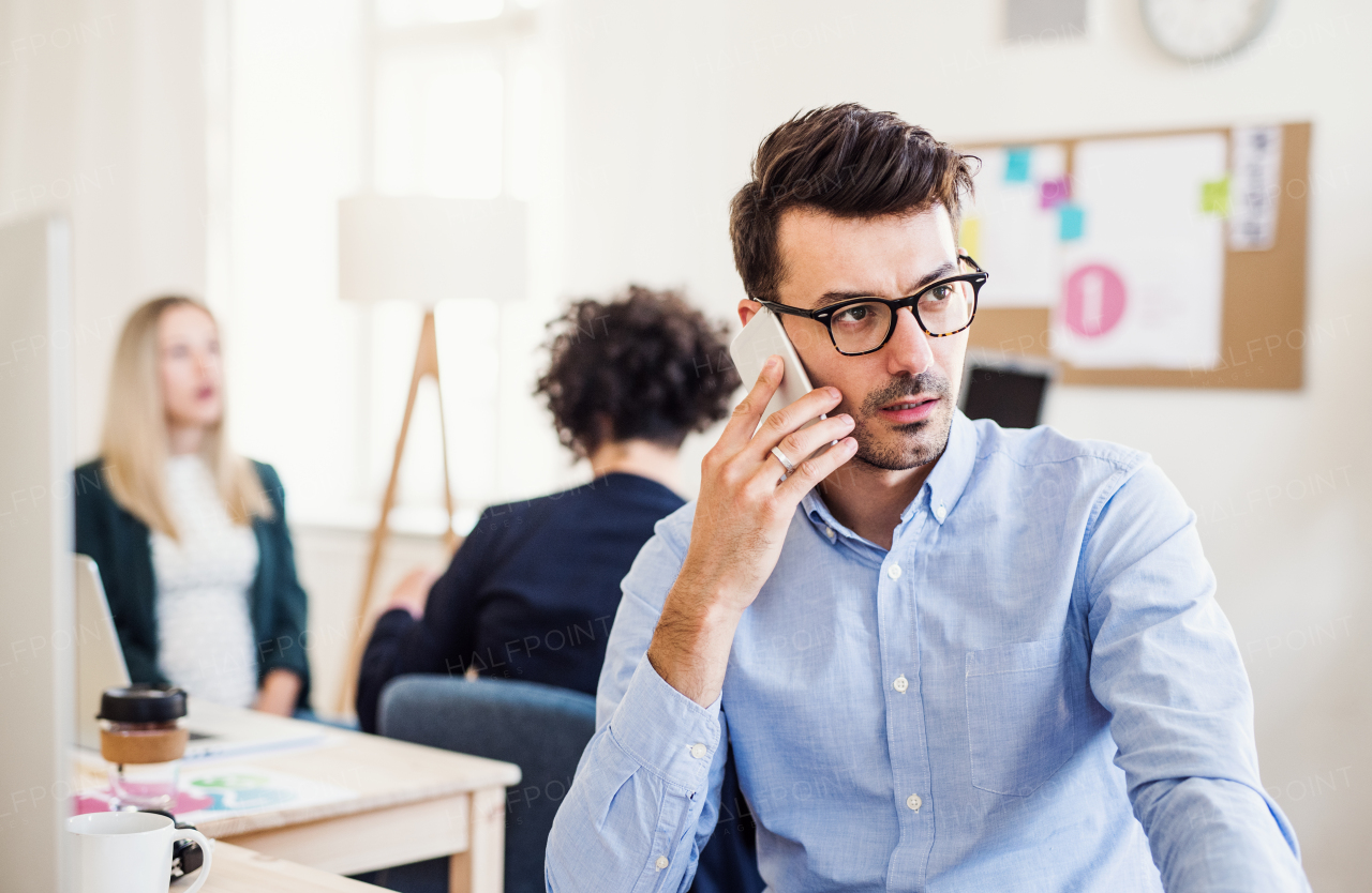 Young businessman with smartphone working in a modern office, making a phone call.