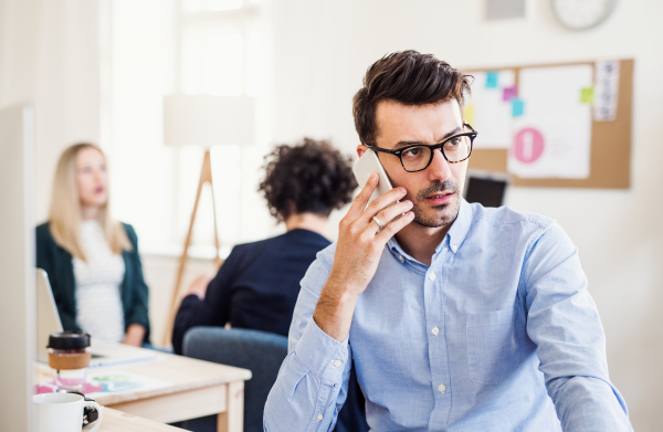 Young businessman with smartphone working in a modern office, making a phone call.