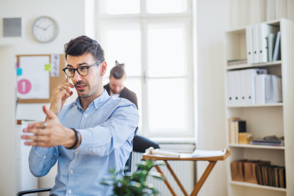 Young businessman with smartphone working in a modern office, making a phone call. Copy space.