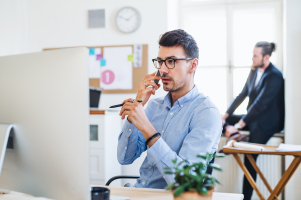 Young businessman with smartphone working in a modern office, making a phone call.