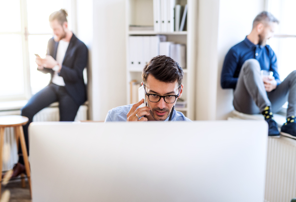 Group of young, cheerful, male businesspeople with computer and smartphone working together in a modern office.