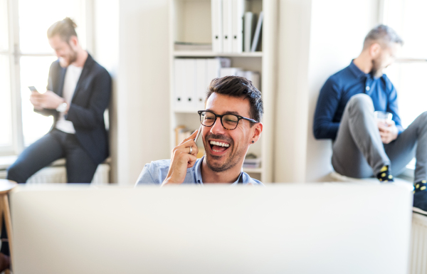 Group of young, cheerful, male businesspeople with computer and smartphone working together in a modern office.