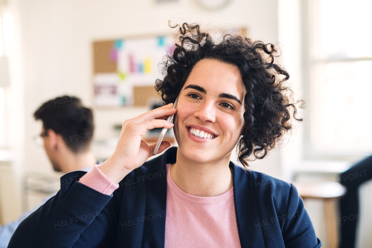 A portrait of young businesswoman with smartphone in a modern office, making a phone call.