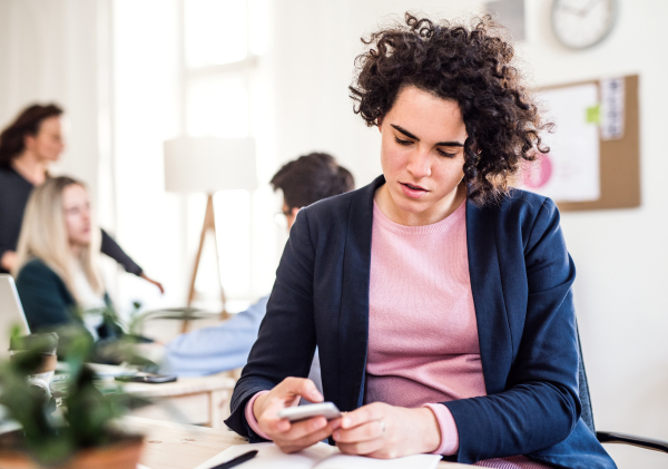 A portrait of young businesswoman with smartphone in a modern office, text messaging.