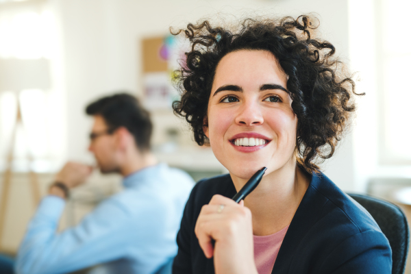 A portrait of young cheerful businesswoman with colleagues in a modern office.