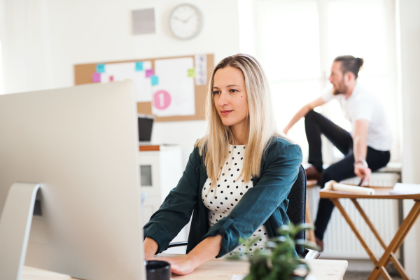 A portrait of young blond businesswoman sitting in a modern office, using computer.