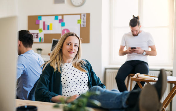 Portrait of young relaxed businesswoman with colleagues in a modern office, feet on desk.