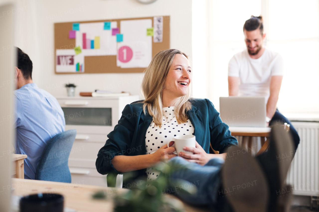 Portrait of young relaxed businesswoman with colleagues in a modern office, feet on desk.