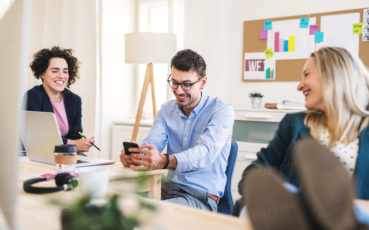 Group of young, cheerful, male and female businesspeople with smartphone working together in a modern office, feet on table.