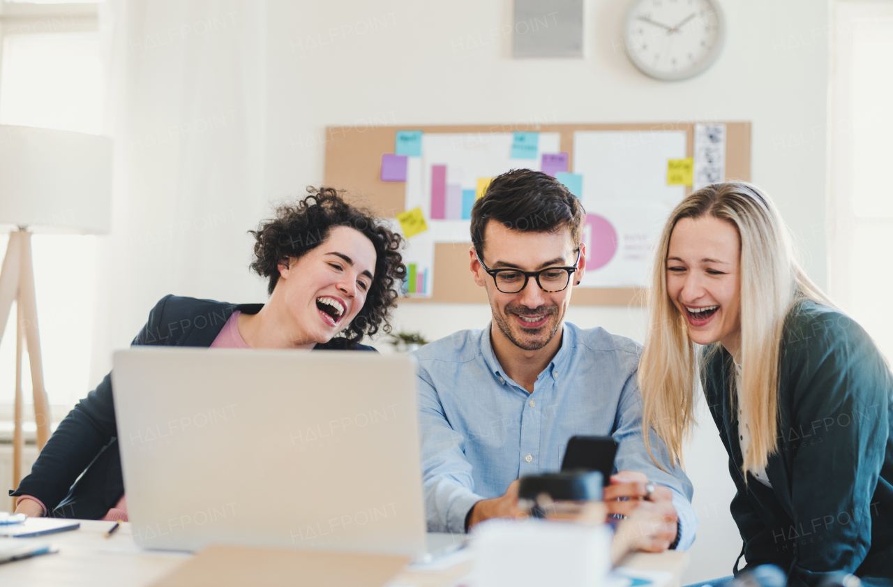 Group of young, cheerful, male and female businesspeople with laptop working together in a modern office.