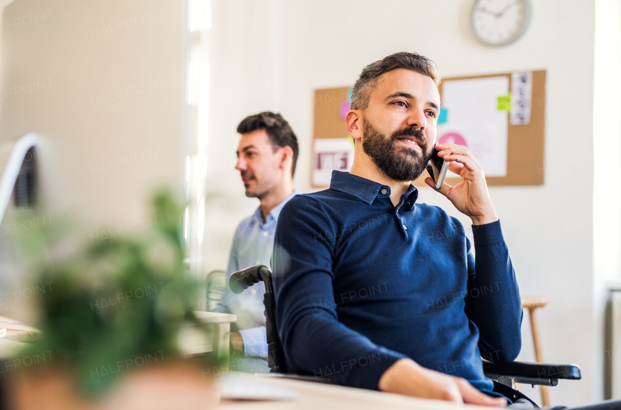 Young businessman in wheelchair with smartphone working in a modern office, making a phone call.