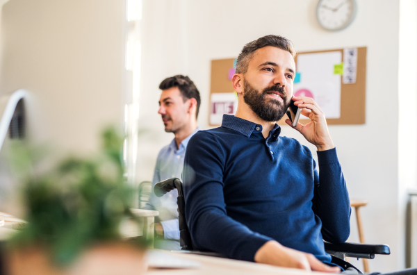 Young businessman in wheelchair with smartphone working in a modern office, making a phone call.