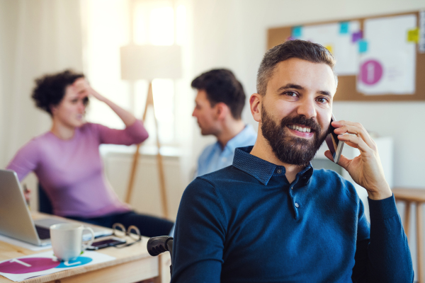 Young businessman in wheelchair with smartphone in a modern office, making a phone call.