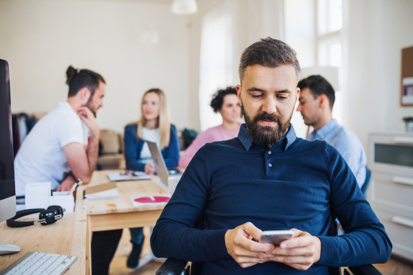 Young businessman in wheelchair with colleagues working in a modern office, using smartphone.