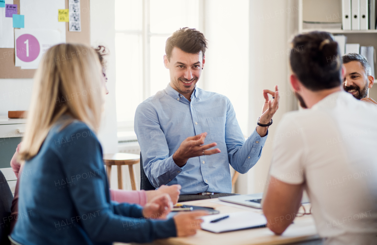 Group of young, cheerful businesspeople sitting around table in a modern office, having meeting.