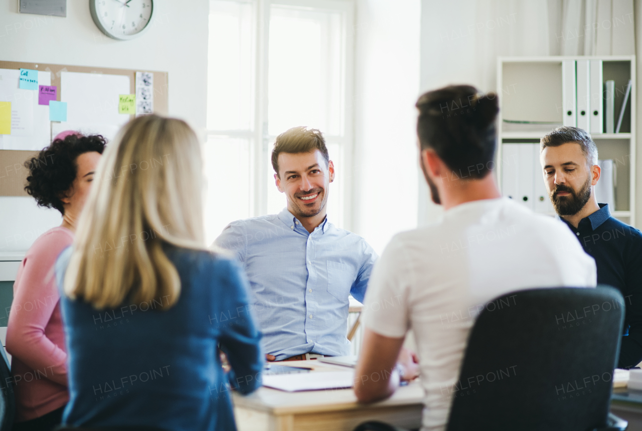 Group of young, cheerful businesspeople sitting around table in a modern office, having meeting.