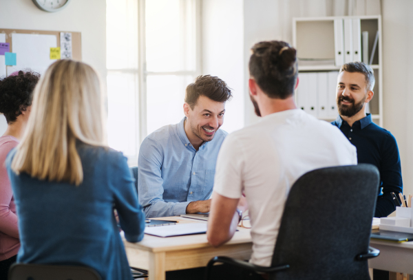 Group of young, cheerful businesspeople sitting around table in a modern office, having meeting.