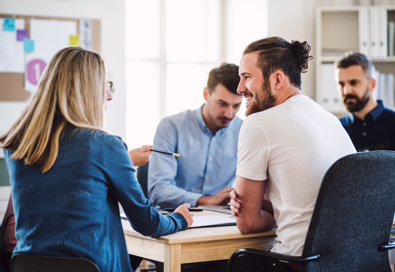 Group of young, cheerful businesspeople sitting around table in a modern office, having meeting.