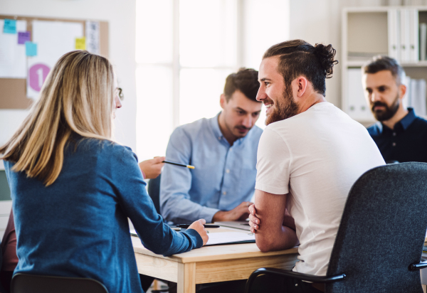 Group of young, cheerful businesspeople sitting around table in a modern office, having meeting.