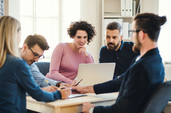 Group of young, cheerful, male and female businesspeople with laptop working together in a modern office.