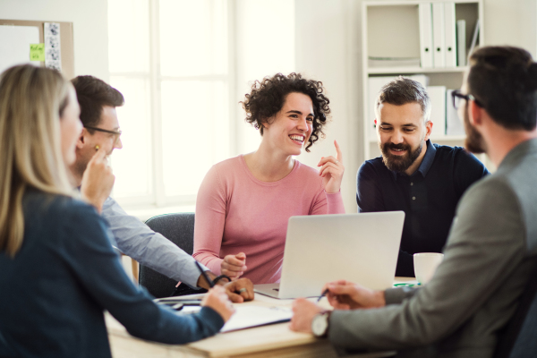 Group of young, cheerful businesspeople sitting around table in a modern office, having meeting.