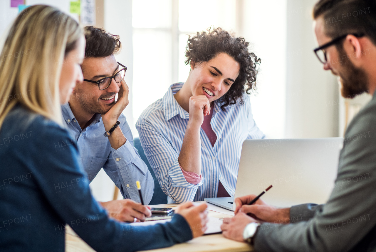 Group of young, cheerful, male and female businesspeople with laptop working together in a modern office.