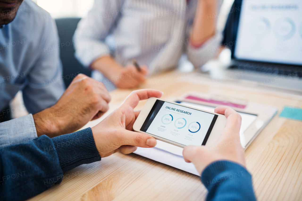 Group of young, male and female businesspeople with smartphone and tablet working together in a modern office, a midsection view.