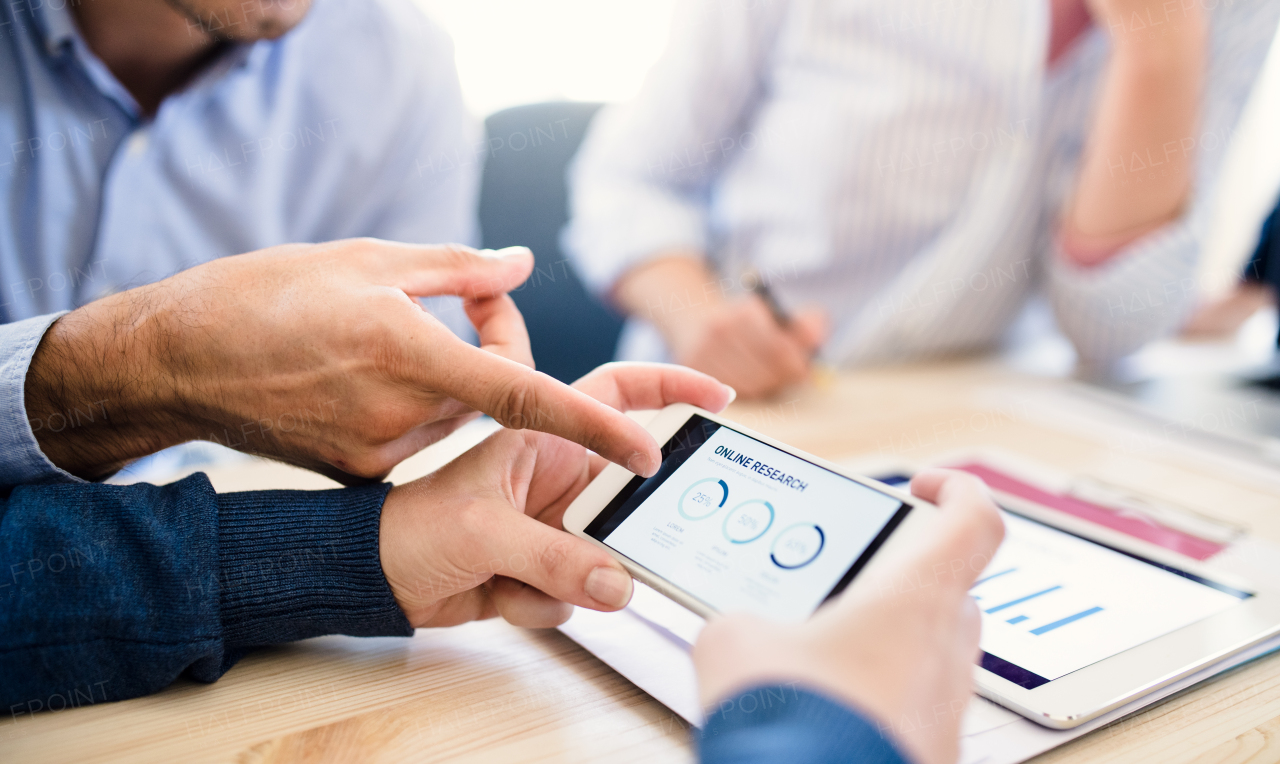 Group of young, male and female businesspeople with smartphone and tablet working together in a modern office, a midsection view.