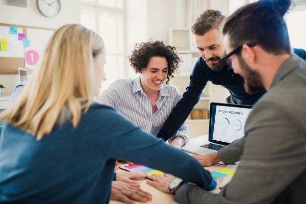 Group of young, cheerful, male and female businesspeople with laptop working together in a modern office.