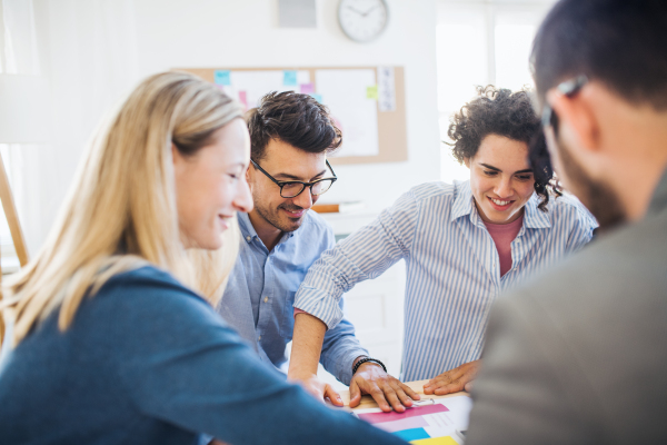 Group of young, cheerful businesspeople sitting around table in a modern office, having meeting.