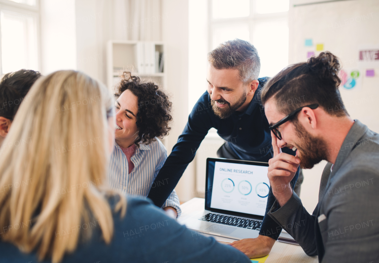 Group of young, cheerful, male and female businesspeople with laptop working together in a modern office.