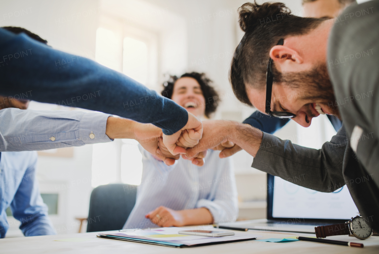 Group of young businesspeople sitting around table in a modern office, making fist bump.