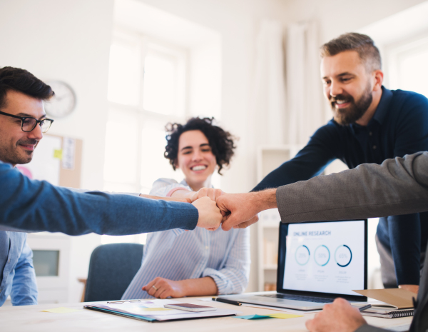 Group of young businesspeople sitting around table in a modern office, making fist bump.