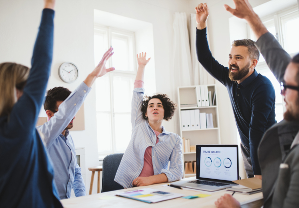 Group of young businesspeople sitting around table in a modern office, celebrating success.