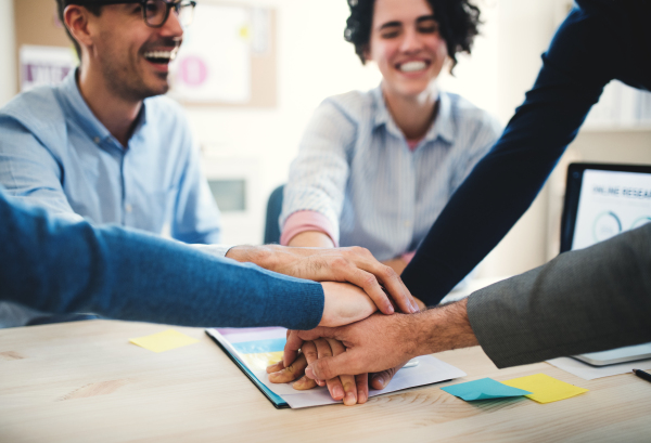 Group of unrecognizable young businesspeople sitting around table in a modern office, stacking hands.