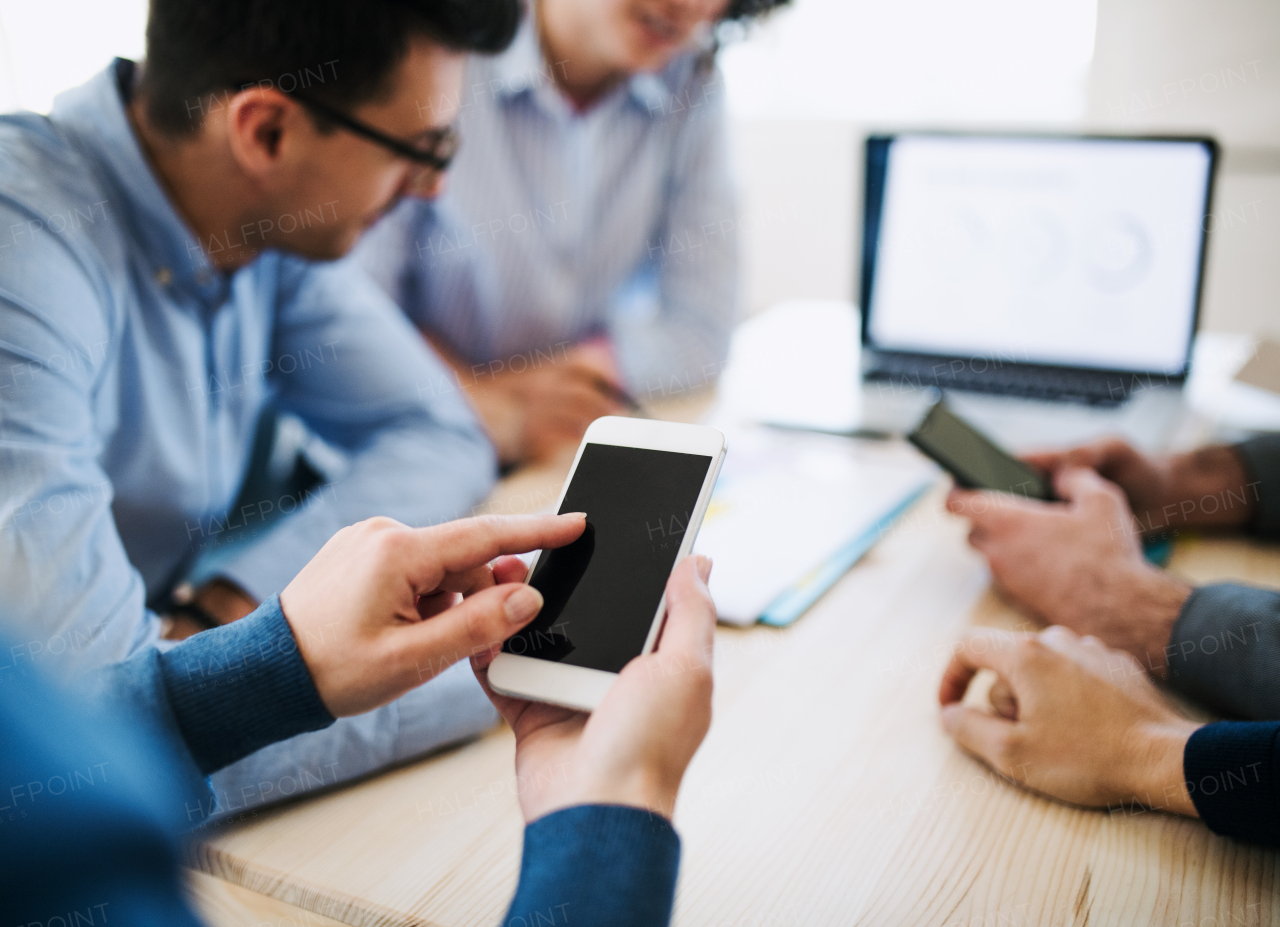 A midsection of group of young businesspeople with smartphone having meeting in office. Copy space.