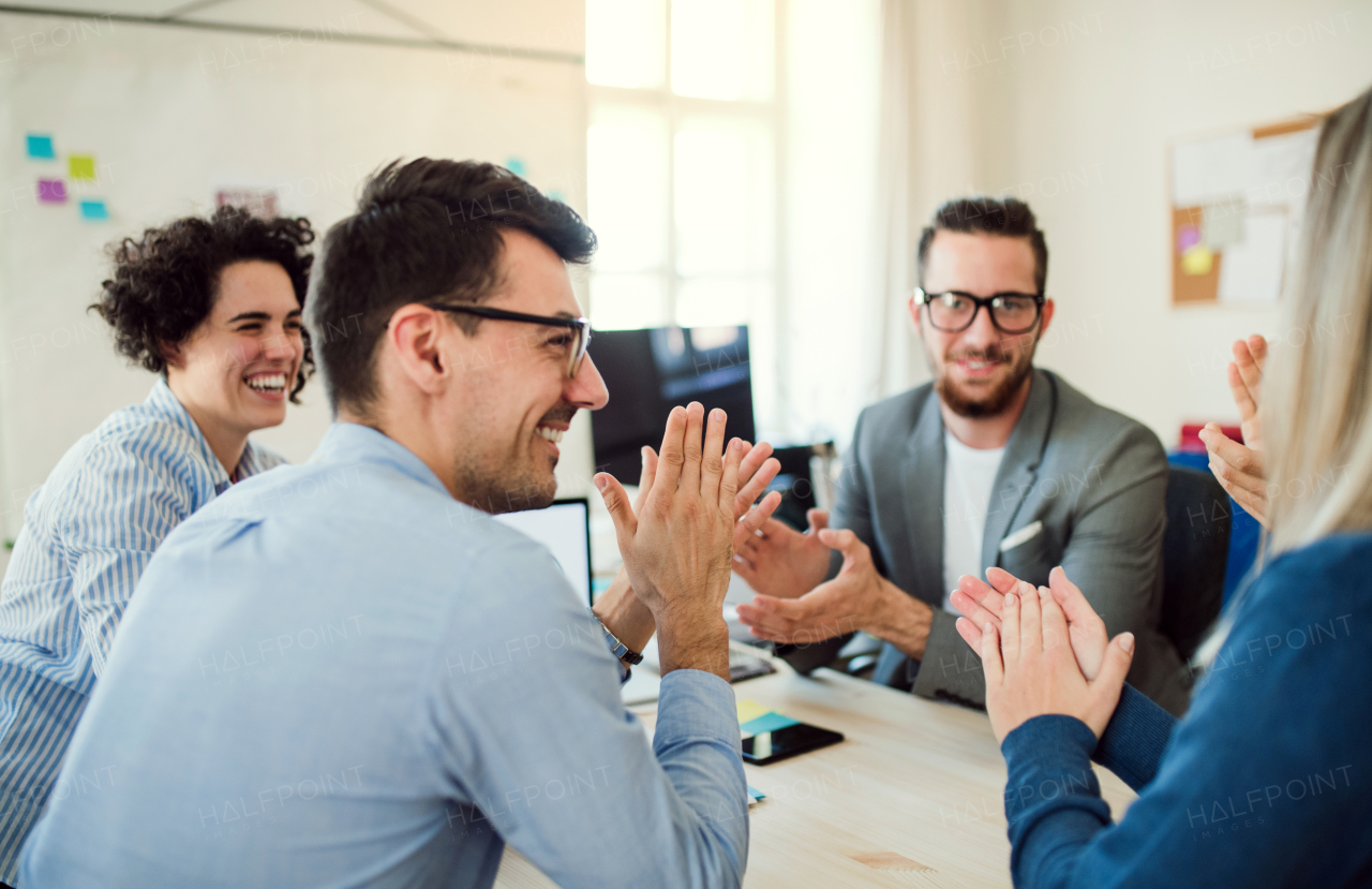 Group of young, cheerful businesspeople sitting around table in a modern office, having meeting.