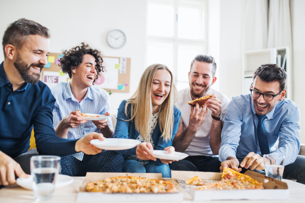 Group of young male and female businesspeople with pizza having lunch in a modern office.