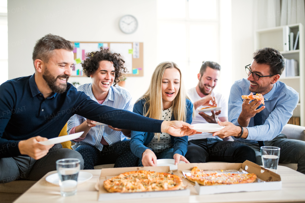 Group of young male and female businesspeople with pizza having lunch in a modern office.