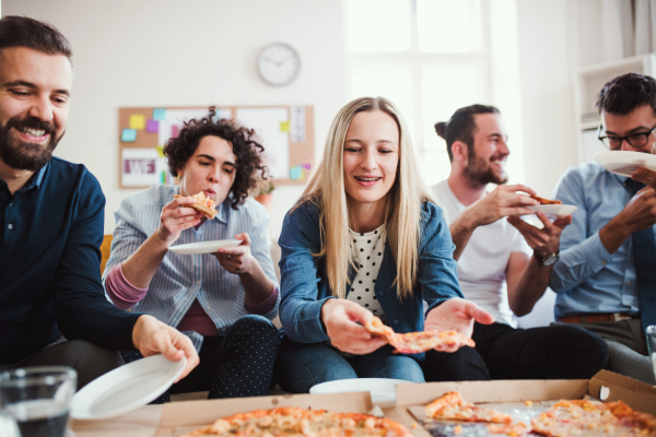 Group of young male and female businesspeople with pizza having lunch in a modern office.