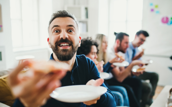 Group of young male and female businesspeople having lunch in a modern office, eating pizza.