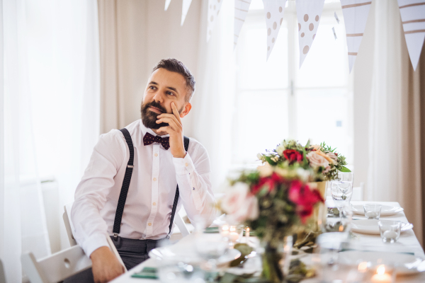 A portrait of a thoughtful hipster mature man standing indoors in a room set for a party.