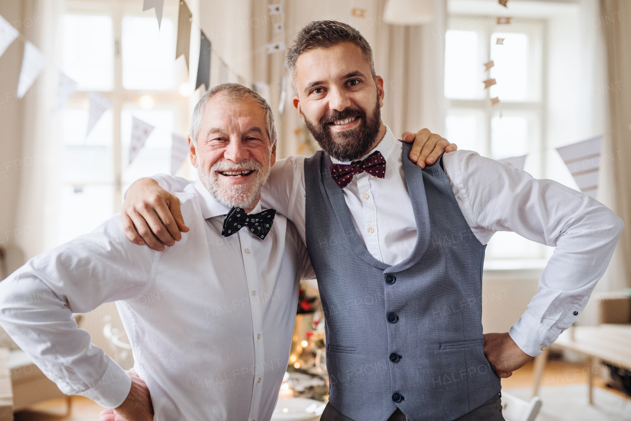 A portrait of a senior and hipster mature man standing indoors in a room set for a party, looking at camera.