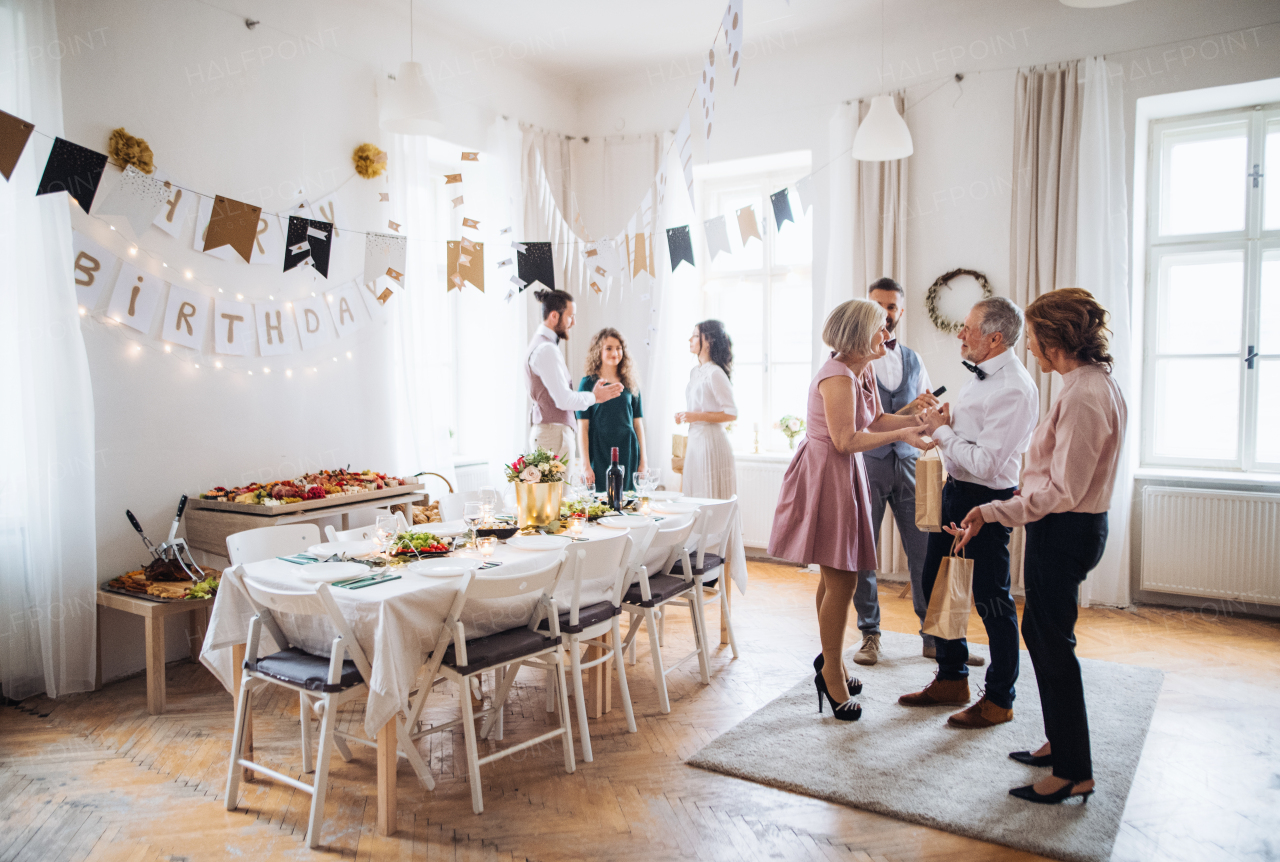 Multigeneration family with presents standing indoor on a birthday party, talking.