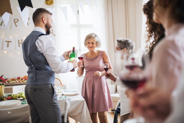 A man pouring happy guests wine on a indoor family birthday party.